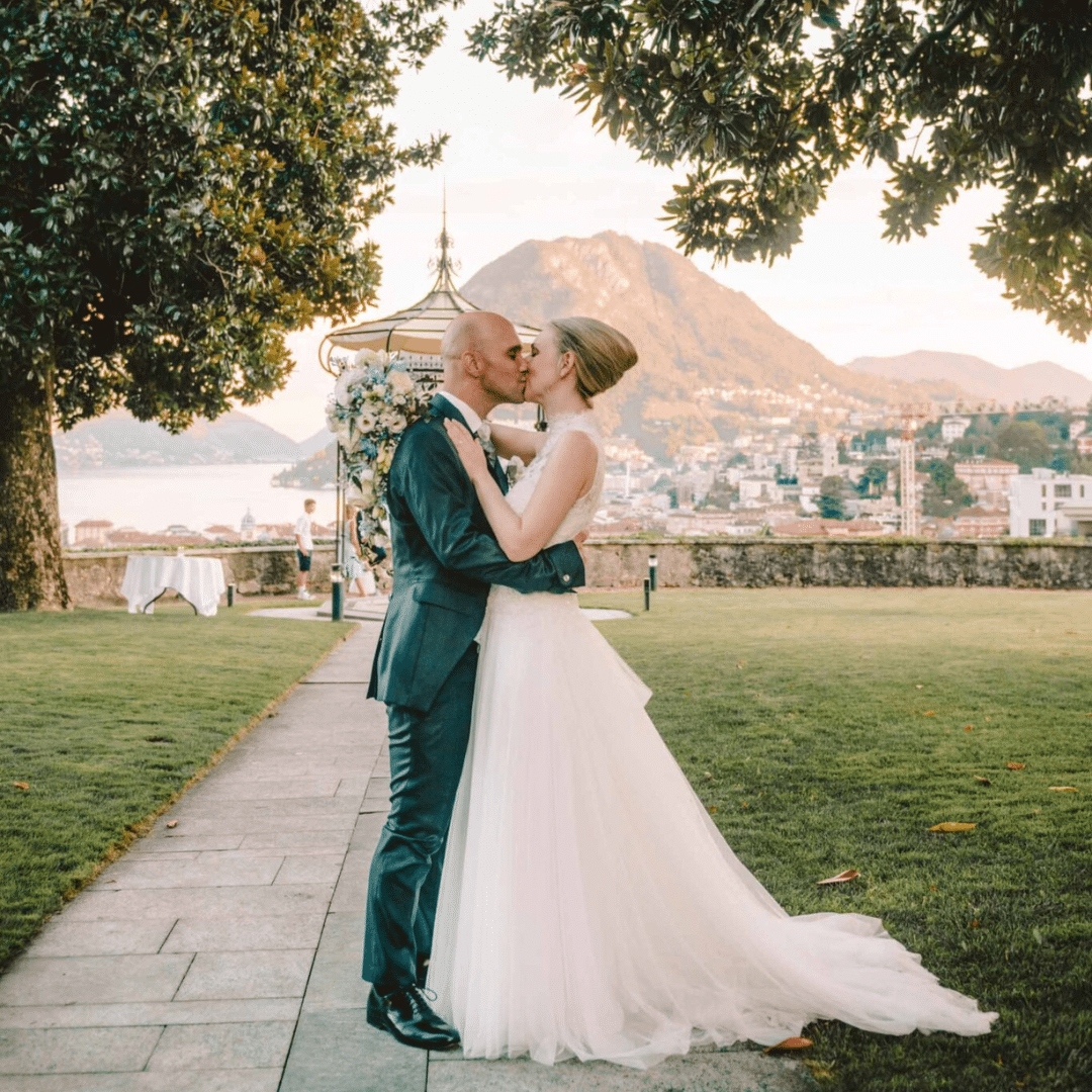 Brautpaar küsst sich im Garten der Villa Sassa. Im Hintergrund sieht man die Aussicht auf den Luganersee.